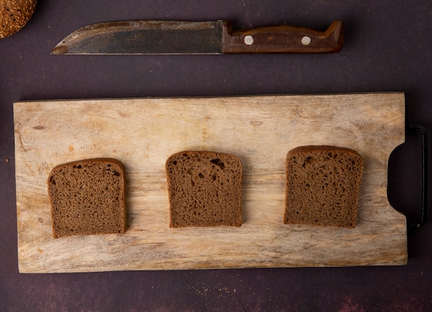 Hoogste mening van de plakken van het roggebrood op scherpe raad met mes op kastanjebruine achtergrond