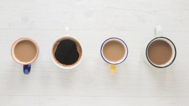 Gratis foto hoogste mening van diverse soorten koffie in koppen die op een rij over wit houten bureau worden geschikt