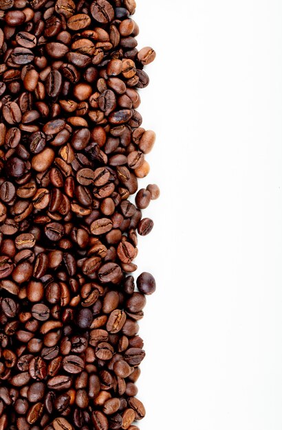Hoogste mening van geroosterde koffiebonen die op witte achtergrond met exemplaarruimte worden verspreid