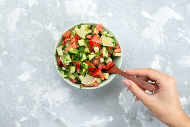 Hoogste meningswijfje die salade mengen met de houten citroen van lepeltomaten en komkommers binnen plaat op wit bureau