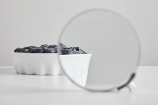 Hoop bosbessen antioxidant biologisch superfood in keramische kom concept voor gezond eten en voeding geïsoleerd op witte tafel, vergroot door verrekijker vergrootglas om details te zien