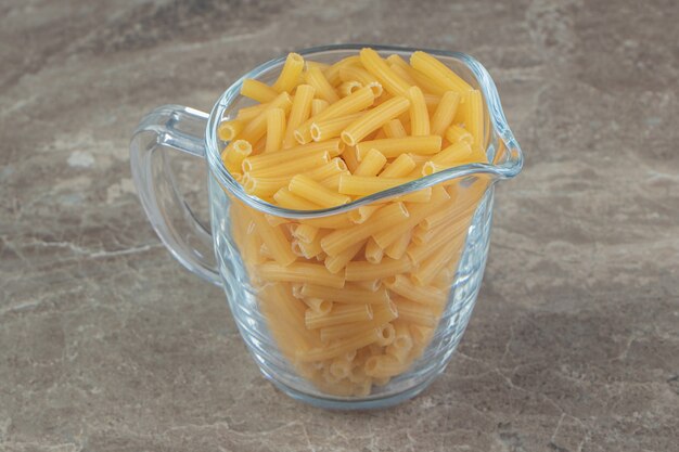Hoop rauwe macaroni in glazen mok.