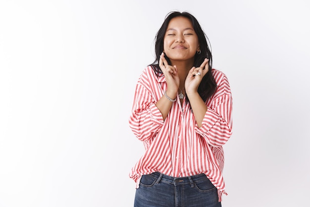 Hoopvolle en optimistische schattige opgewonden aziatische vrouw die vingers kruist