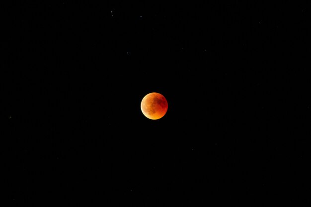 Horizontaal lang schot van een oranje en rode maan in de donkere hemel bij nacht