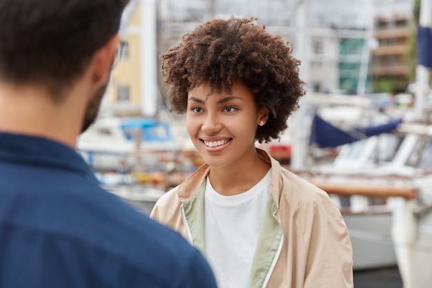 Horizontaal schot van aantrekkelijk afro-amerikaans meisje heeft een prettige uitstraling, brede glimlach