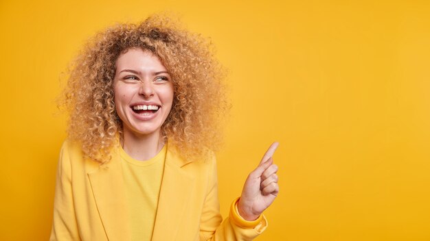 Horizontaal schot van een gelukkige vrouw met krullend haar die tandjes glimlacht, geeft aanbeveling