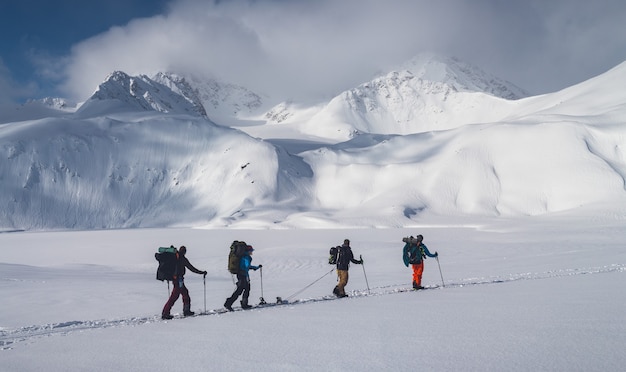 Horizontaal schot van een groep mensen die wandelen in de bergen bedekt met sneeuw onder de bewolkte hemel