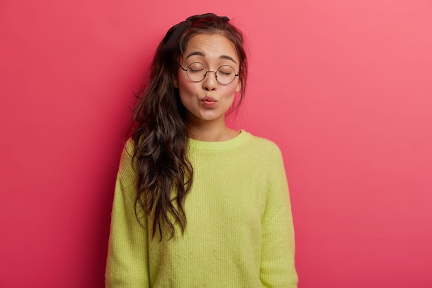 Gratis foto horizontaal schot van mooie donkerbruine aziatische vrouw met afgeronde lippen, houdt de ogen dicht