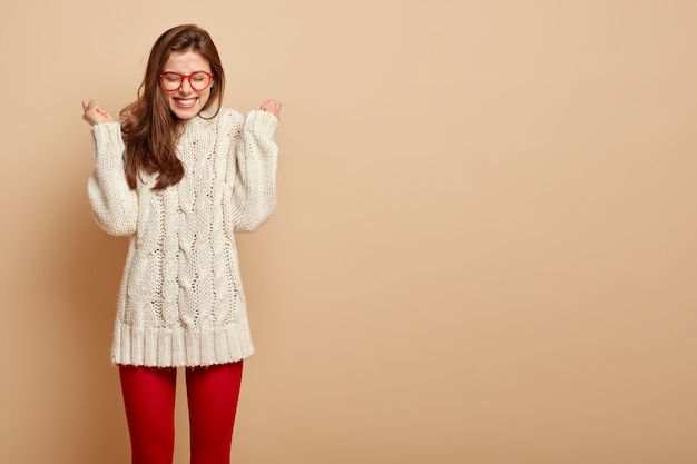 Horizontaal schot van positieve europese vrouw drukt positieve emoties uit, heft gebalde vuisten op, lacht om iets