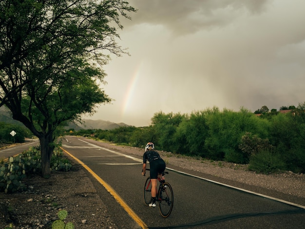 Horizontale foto van vrouwelijke fietser in beweging die een fiets op de weg over de natuur rijdt