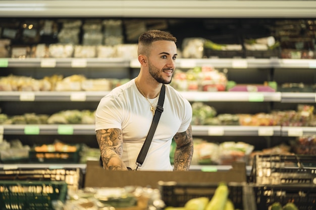 Horizontale ondiepe focus van een man die vrolijk naar iets in de supermarkt kijkt