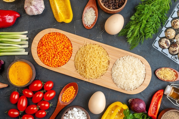 Horizontale weergave van dinerbereiding met verse groenten, verschillende kruiden, groene bundels, gevallen oliefles, brood, sneetjes, eieren, op donker
