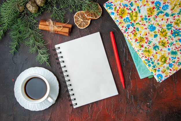 Horizontale weergave van een kopje zwarte thee gesloten notitieboekje met pen, kaneellimoenen, een bal touw en boeken op een donkere achtergrond