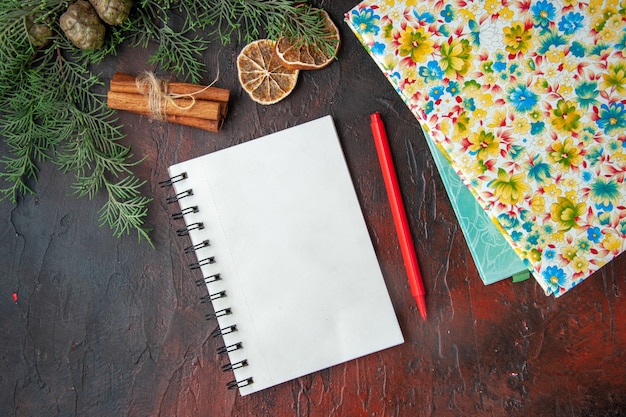 Horizontale weergave van gesloten notitieboekje met pen, kaneellimoenen, een bal van touw en boeken op een donkere achtergrond