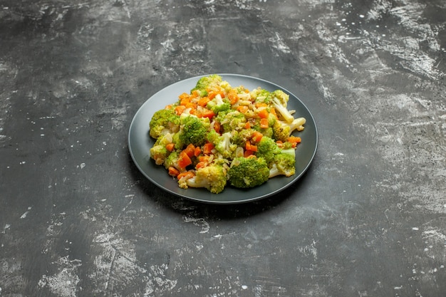 Horizontale weergave van gezonde maaltijd met brocoli en wortelen op een zwarte plaat op grijze tafel