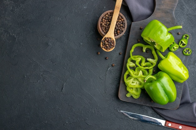 Horizontale weergave van hele gesneden gehakte groene paprika's op houten snijplank op donkere kleur oppervlak color