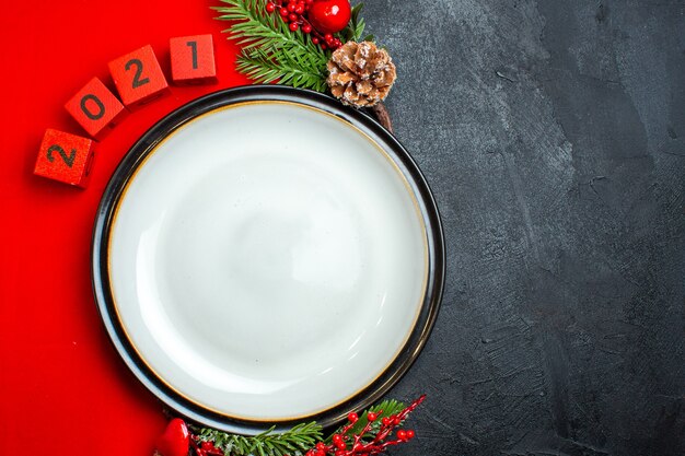 Horizontale weergave van Nieuwjaar achtergrond met diner plaat decoratie accessoires fir takken en getallen op een rood servet op een zwarte tafel