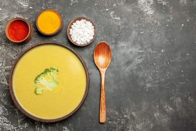 Horizontale weergave van romige broccolisoep in een bruine kom verschillende kruiden en lepel op grijze tafel