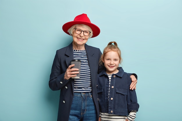 Gratis foto horizontale weergave van vrolijke grootmoeder draagt stijlvolle rode hoed, zwarte jas