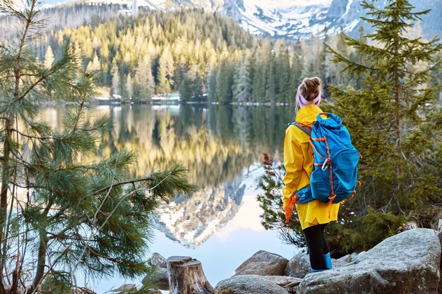 Horizontale weergave van vrouwelijke toerist geniet van rustige afgelegen bergzicht op het meer, staat terug naar de camera