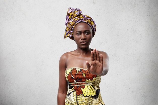 Hou op! Afrikaanse vrouw met donkere gladde huid die traditionele kleding draagt die haar handpalm toont en ontkent iets niet te doen. Zelfverzekerd donkerhuidig vrouwtje zonder gebaar. Veto en vraagconcept