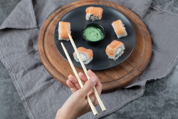 Houd een zalmsushi-rolletje met stokjes.