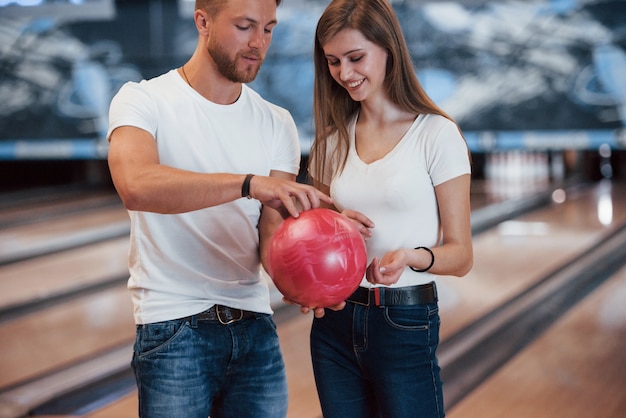 Houd het op die manier vast. Man die meisje leert hoe ze de bal moeten vasthouden en bowlen in de club