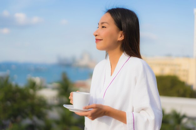 Houdt de portret mooie jonge Aziatische vrouwen koffiekop rond openluchtmening in hand