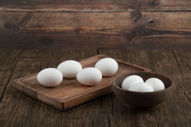 Houten bord en kom vol biologische rauwe eieren op houten achtergrond.