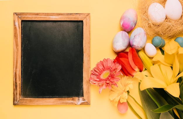 Gratis foto houten bord met paaseieren en verse bloemen op gele achtergrond