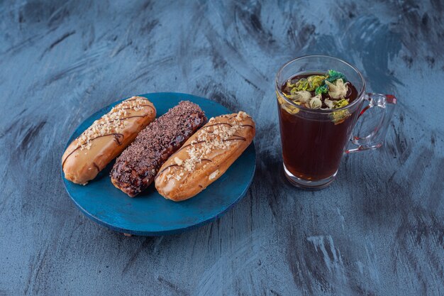 Houten bord met verschillende zoete eclairs en kopje thee op marmeren oppervlak.