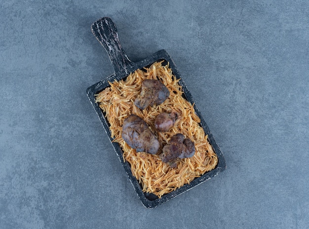 Houten bord pasta met droog vlees op stenen oppervlak.