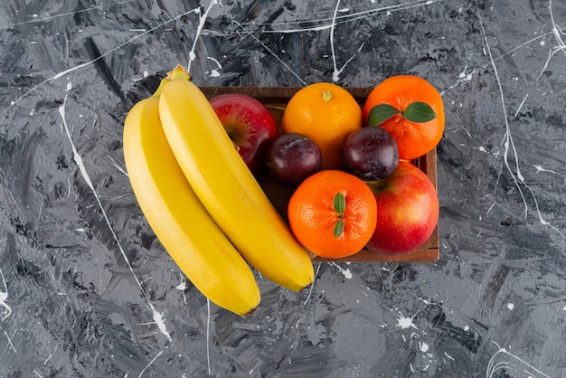 Houten kist vol met vers fruit op marmeren oppervlak.