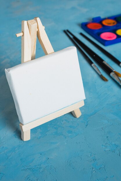 Houten kleine witte lege ezel met penseel op blauwe gestructureerde achtergrond
