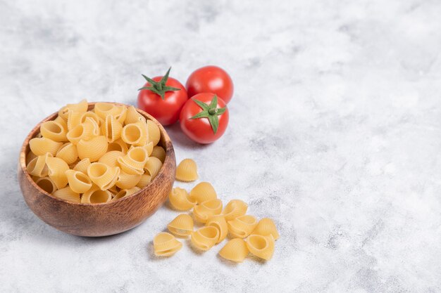 Houten kom vol met ongekookte pasta Conchiglie geplaatst op marmeren achtergrond. Hoge kwaliteit foto