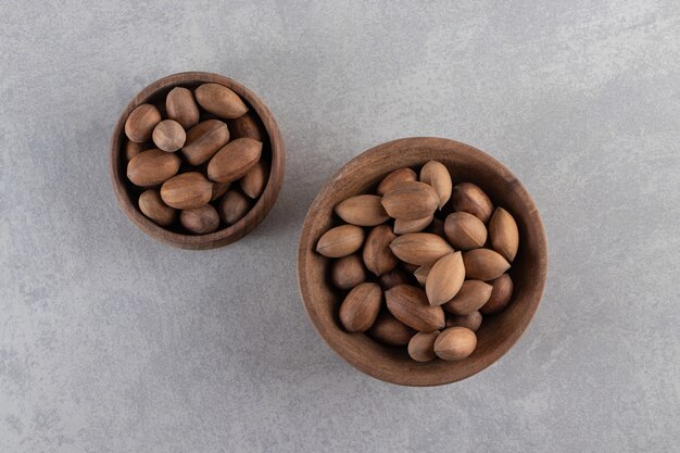 Houten kommen van biologische gepelde walnoten op stenen achtergrond.
