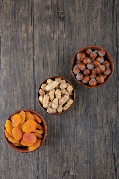 Houten kommen vol gezonde noten met gedroogde abrikozenvruchten op houten tafel.