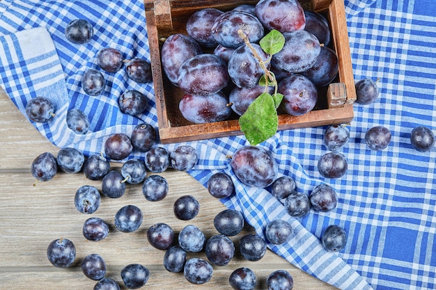 Houten mandje met tuinpruimen op een houten tafel met een tafellaken. Hoge kwaliteit foto