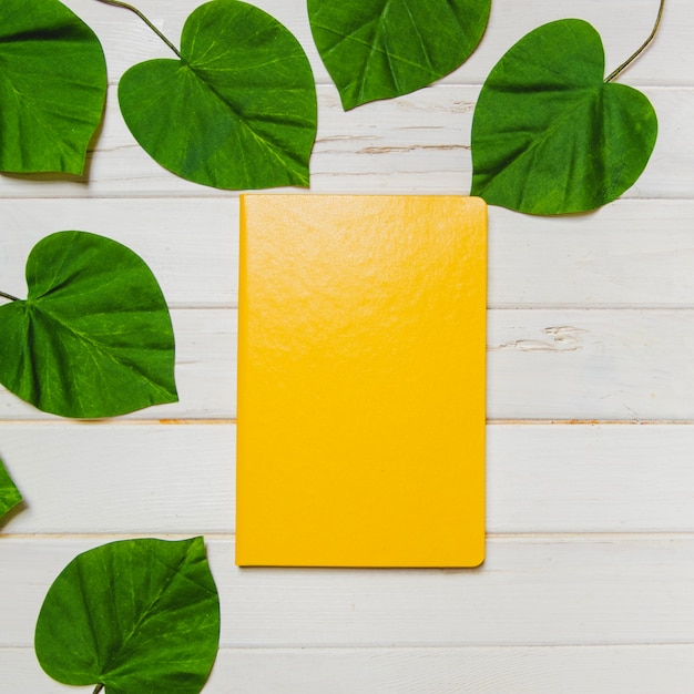 Gratis foto houten oppervlak met gele notitieboekje en groene bladeren