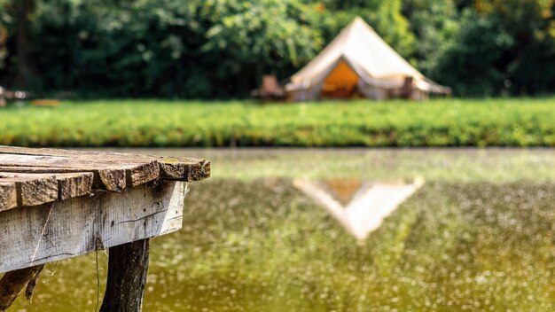 Houten pier voor rust in de buurt van een meer met tent op de achtergrond bij glamping. Natuur, groen rondom