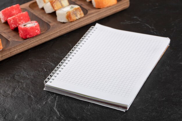 Houten plaat met traditionele sushibroodjes en notitieboekje op zwarte tafel