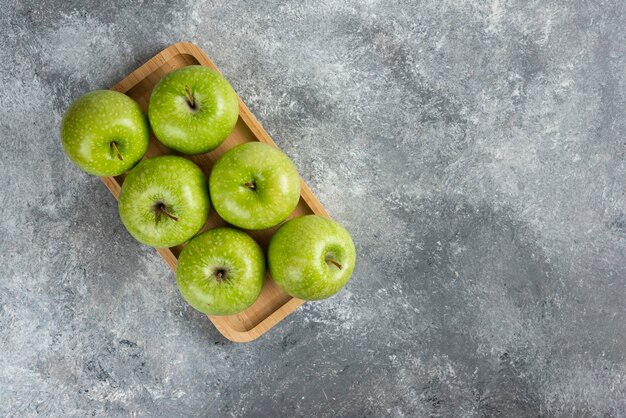 Houten plaat van glanzende groene appels op marmeren tafel.