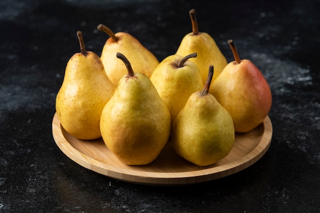 Houten plaat van smakelijke gele peren op zwarte ondergrond.