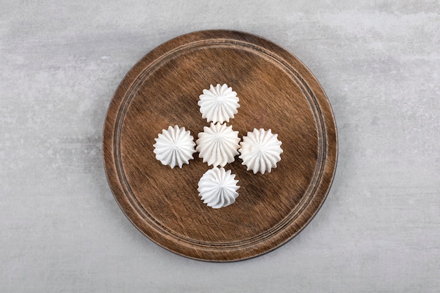 Houten plaat van wit meringue dessert op stenen tafel.