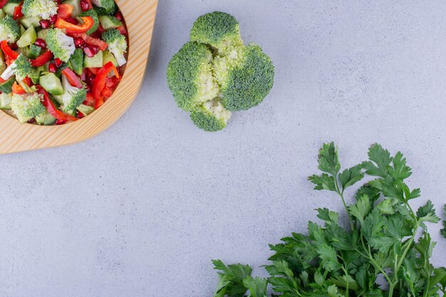 Houten schotel van salade met bundels broccoli en peterseliebladeren op marmeren achtergrond. Hoge kwaliteit foto