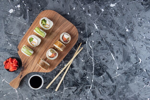 Houten snijplank van verschillende sushi rolt op marmeren tafel.