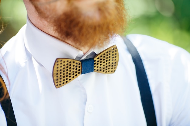 Houten vlinderdas over het witte shirt onder rode baard