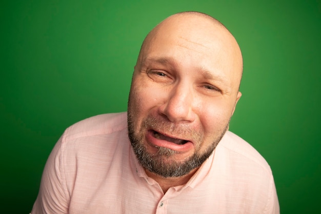 Gratis foto huilen recht vooruit kijken kale man van middelbare leeftijd met roze t-shirt geïsoleerd op groen