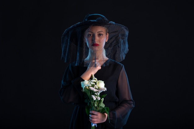 Huilende vrouw gekleed in het zwart met bloemen op een zwarte droefheid begrafenis dood