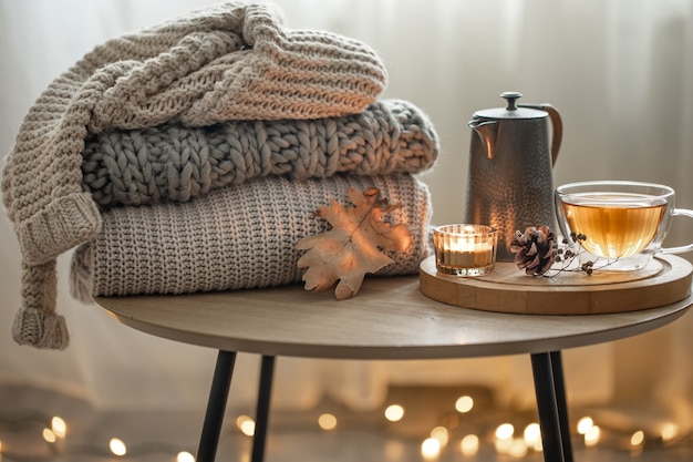 Huis herfst compositie met thee en gebreide truien in het interieur van de kamer, op een onscherpe achtergrond met een slinger.